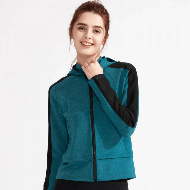 Smiling woman wearing a blue women's hooded sweatshirt with zipper, featuring long sleeves and thumb holes, ideal for sports.